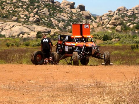 1996 Ford Bronco - A man stands next to an orange off-road buggy with the number 103 displayed prominently.