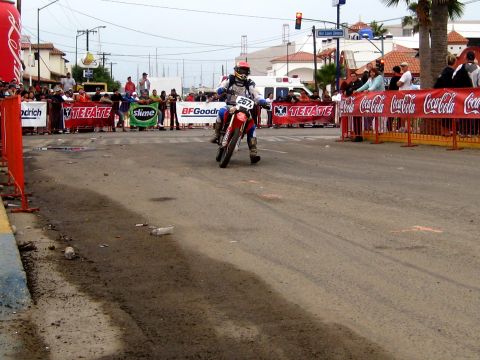 1996 Ford Bronco - A motorcycle racer speeds through a street course, with crowds watching from behind sponsor barriers.