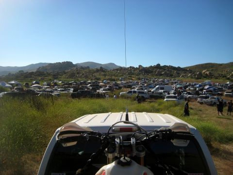 1996 Ford Bronco - A vast number of vehicles are parked in a field under a clear blue sky, with mountains in the background.