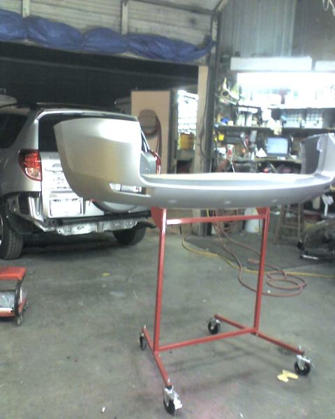 1993 Ford C-350 (Centurion Conversions) - Silver rear bumper on a red rolling stand in a workshop, with a silver SUV in the background.