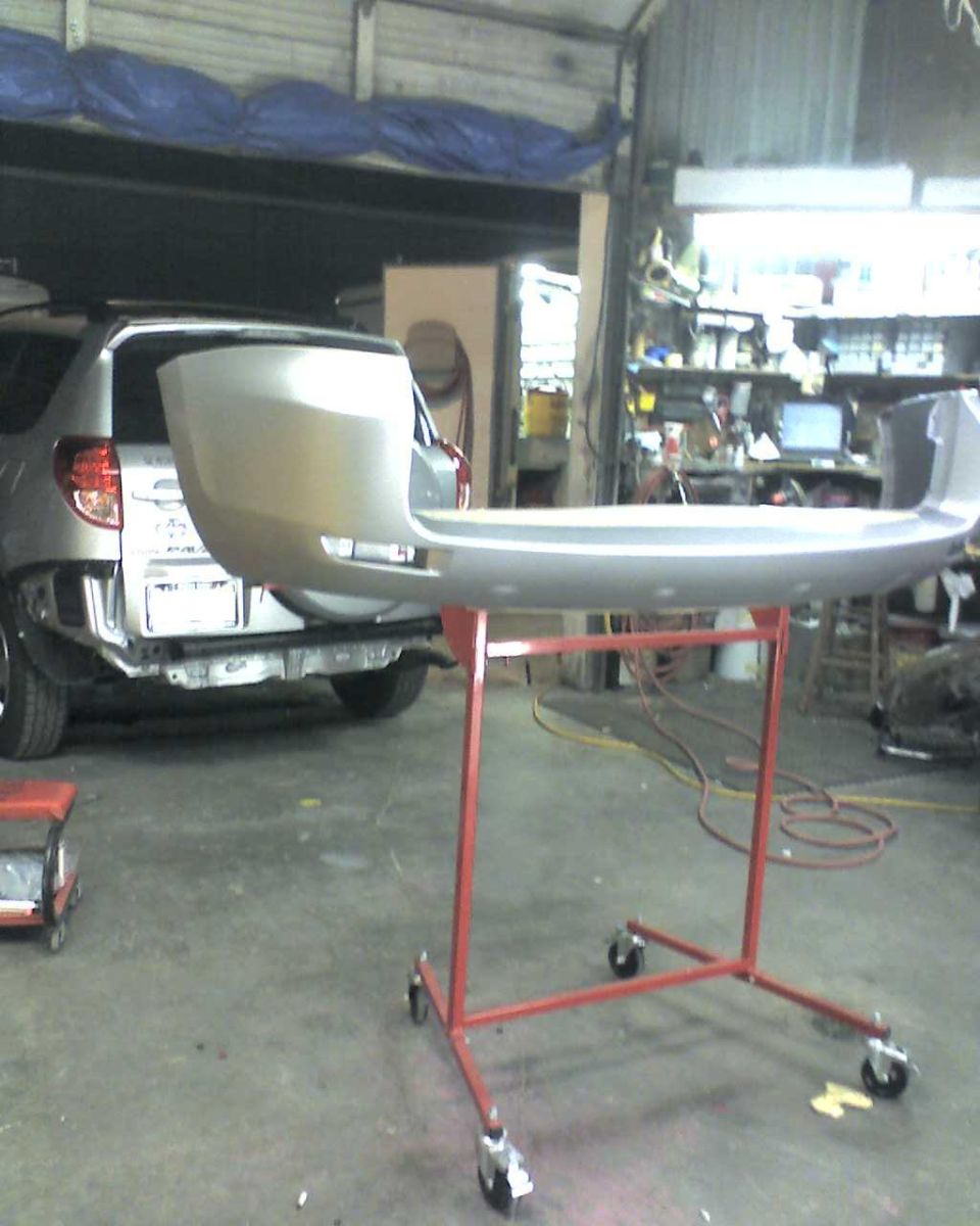 Silver rear bumper on a red rolling stand, with the rear of a silver SUV visible behind it