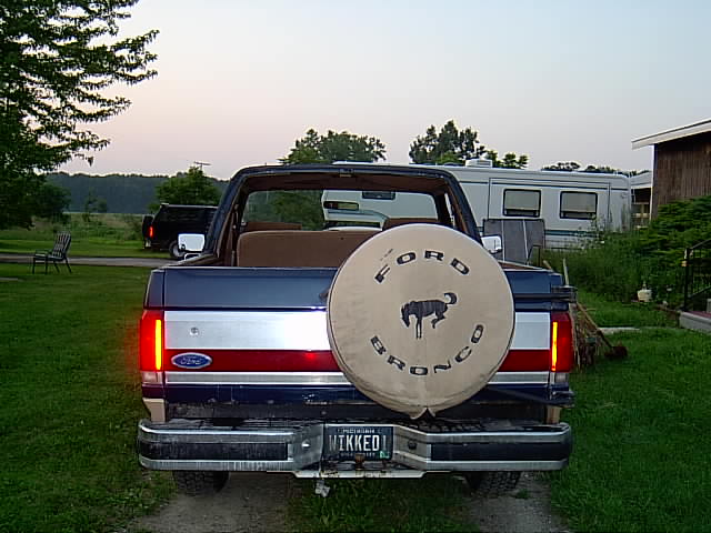 Rear of a dark blue Ford Bronco, top removed, tan Ford Bronco spare tire cover, Michigan plate WIKKED