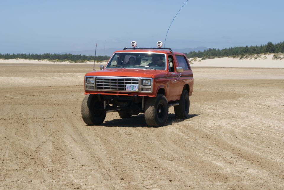 Orange Ford Bronco with lifted suspension and large tires on a sandy beach, license plate 419 EPJ