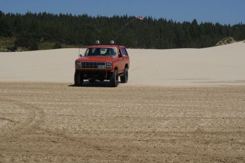 1983 Ford Bronco - This orange 1983 Ford Bronco is captured in a front-facing view as it navigates sandy terrain, complete with an antenna flag.