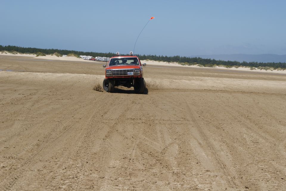 Orange SUV driving on a sandy beach with dunes in the background