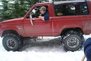 1983 Ford Bronco - Red 1983 Ford Bronco navigates a snowy terrain with a driver inside.