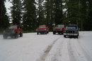 1983 Ford Bronco - Several vehicles are parked on a snow-covered ground, surrounded by trees.