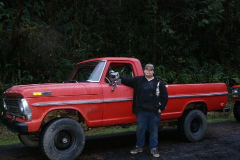 1983 Ford Bronco - A man poses with a classic red pickup truck, with another vehicle in the background.