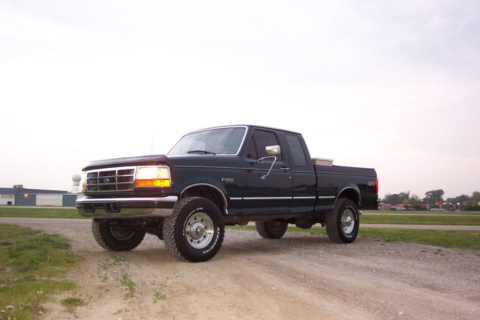 Dark green 1997 Ford F-250 truck with chrome accents and off-road tires parked on a dirt road