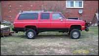 1991 GMC Suburban - Side view of a red 1991 GMC Suburban with a lifted suspension and black trim.