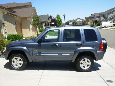 2002 Jeep Liberty - A gray 2002 Jeep Liberty SUV is parked on a paved driveway in front of a house.