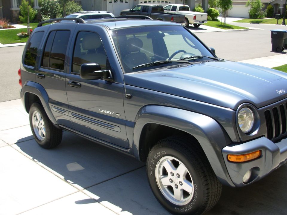 Dark blue 2002 Jeep Liberty parked in driveway with two pickup trucks behind it