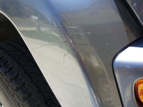 2002 Jeep Liberty - Scratches mar the gray body panel of a vehicle, with a tire visible in the foreground.