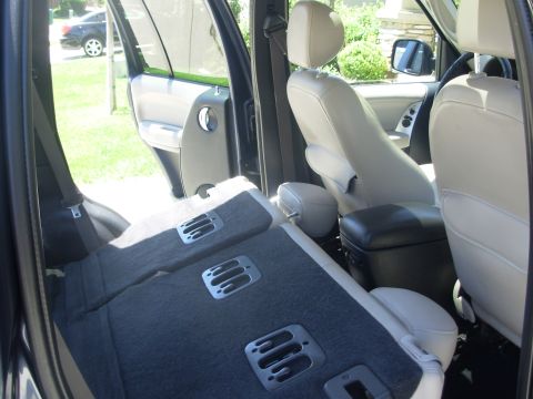 2002 Jeep Liberty - The interior of a vehicle shows folded rear seats and light-colored front seats, with the driver's side door open.