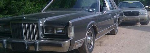 2000 Mercury Grand Marquis - A dark gray sedan is parked in front of another vehicle on a dirt road.