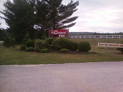 1990 Ford Bronco - The entrance to the Oxford Fair is marked by a large red sign, with a white fence and fields visible beyond.