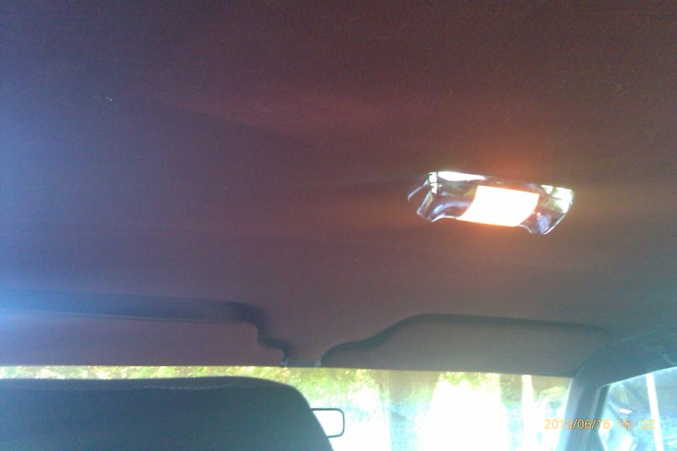Car interior ceiling with dome light on. Sun visors visible. Supermotors.net logo in corner