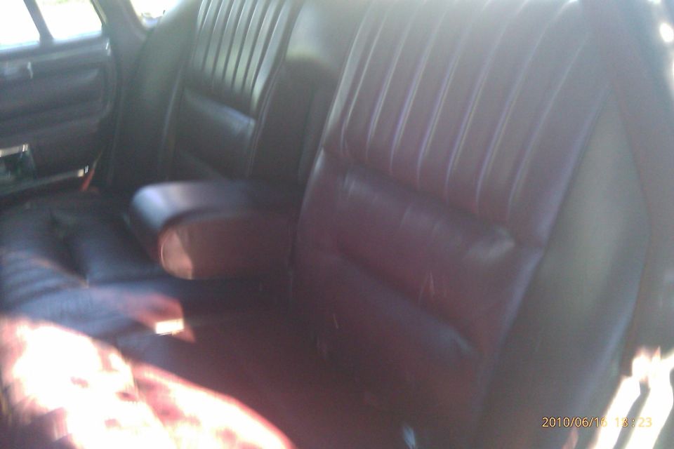 Dark leather rear car seats with a center armrest. Sunlight streams in from the right