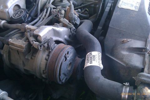 2000 Mercury Grand Marquis - Close-up view of an engine bay, highlighting the AC compressor and a curved radiator hose with visible part information.