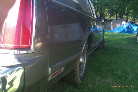 2000 Mercury Grand Marquis - The rear of a classic Lincoln sedan is shown from a low angle, with a blue tarp and shed in the background.