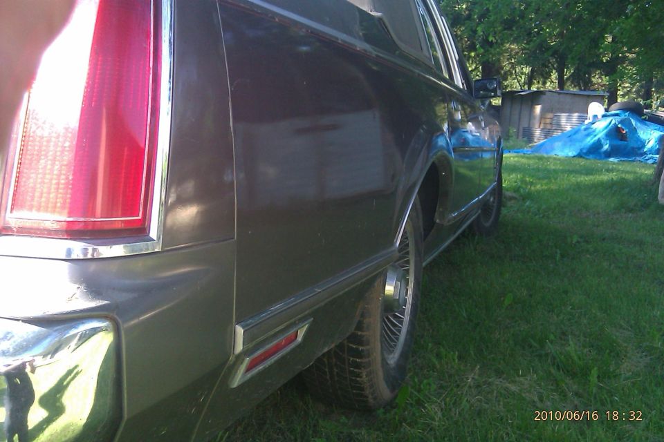Rear quarter panel and taillight of a dark-colored 1980s Lincoln Town Car parked on grass