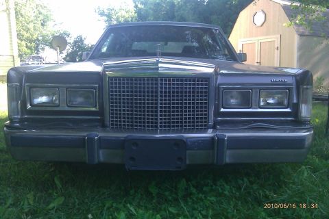 2000 Mercury Grand Marquis - This Lincoln Town Car features a prominent grille and dual headlights, with a shed visible behind it.
