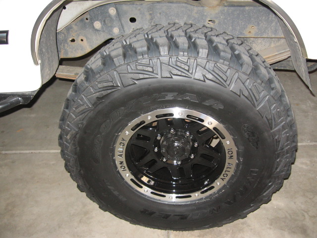 Black ION Alloy wheel with Goodyear Wrangler mud tire leaning in garage