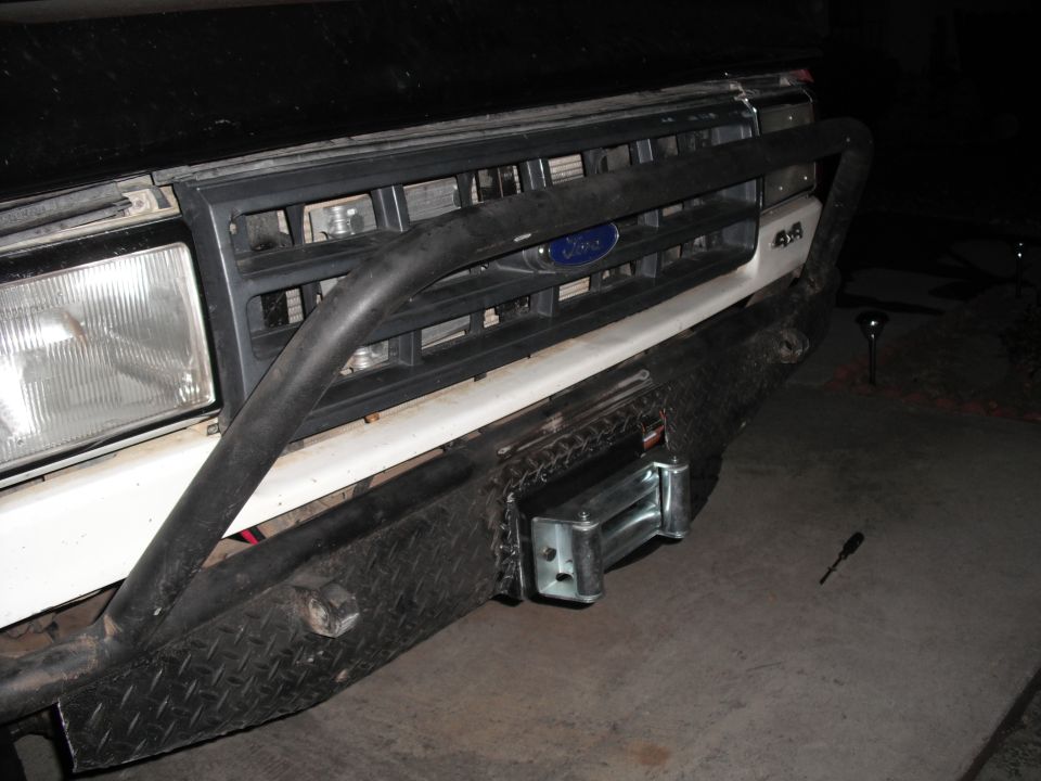 Front bumper with winch on a 1987 Ford Bronco, showing a black grille and diamond plate bumper