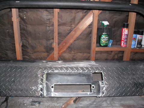 1991 Ford Bronco - A custom bumper with a winch mount is shown in a workshop setting, with cleaning supplies and spray paint on a shelf behind it.