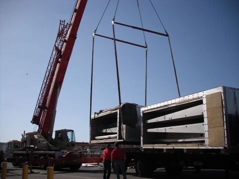 1991 Ford Bronco - A large crane is in the process of lifting heavy industrial equipment off a flatbed truck.