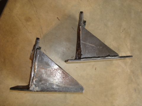 1995 Ford Bronco - Two custom-fabricated metal brackets are shown, likely for automotive use, resting on a textured surface.