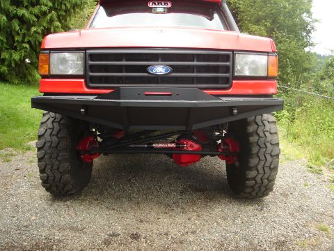 1989 Ford Bronco - Custom bumper and suspension on a red Ford truck, likely from the late 1980s.