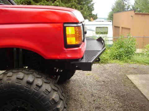 1989 Ford Bronco - A red pickup truck is shown from the front corner, a custom black bumper and large off-road tires.
