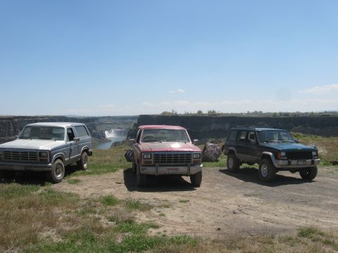 1981 Ford Bronco - Three SUVs are parked on a dirt road overlooking a waterfall on a clear day.