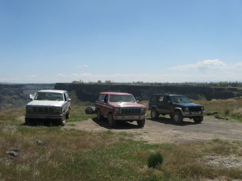 1981 Ford Bronco - Three SUVs, including a 1980s Ford Bronco, are parked on a dirt road with a canyon view.