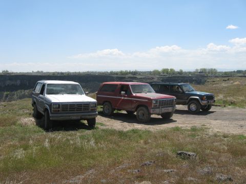 1981 Ford Bronco - Three SUVs parked on a dirt road overlooking a canyon on a sunny day.