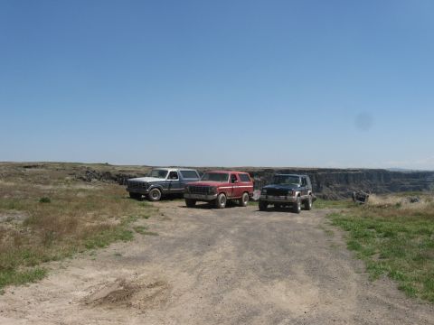 1981 Ford Bronco - Three SUVs, including a 1981 Ford Bronco, are parked on a dirt road with a canyon vista.