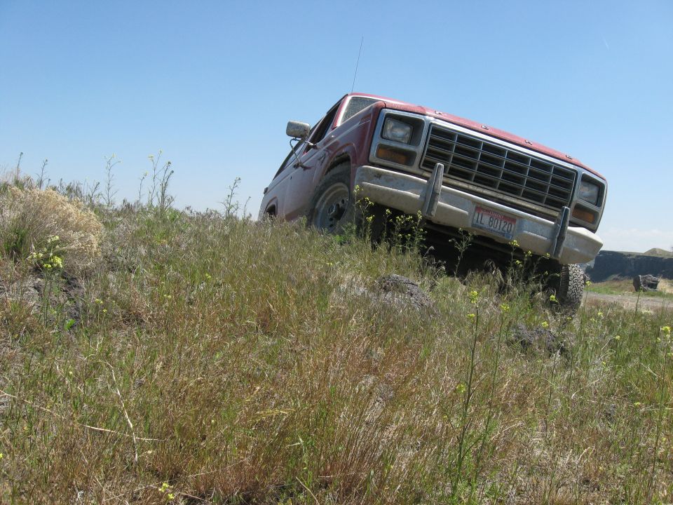 Red 1980 Ford Bronco on grassy hill, front 3/4 view