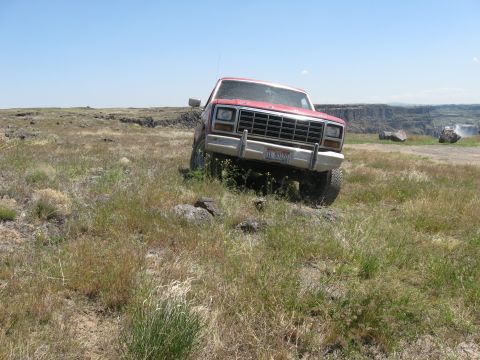1981 Ford Bronco - Red pickup truck navigating off-road terrain with a canyon in the background.