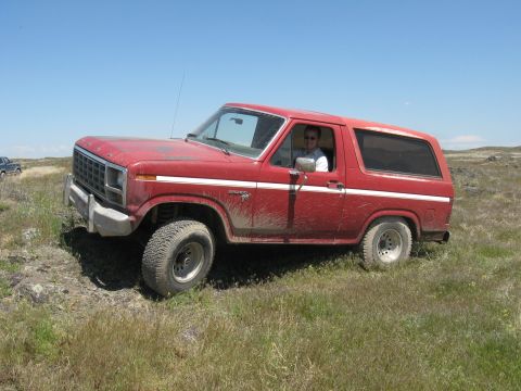 1981 Ford Bronco - A red Ford Bronco drives off-road under a clear blue sky.