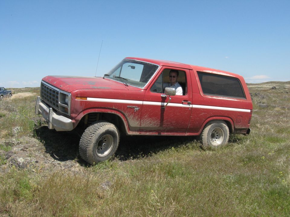 Red Ford Bronco with white side stripe, driver visible, off-road tires, on grassy terrain