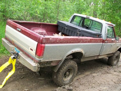 1988 Ford F-150 - This Ford pickup truck appears to be stuck in a muddy, wooded area, with a tow strap attached to its rear bumper.