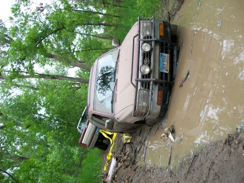 1988 Ford F-150 - A truck is stuck in a muddy rut with another vehicle visible behind it, surrounded by trees.