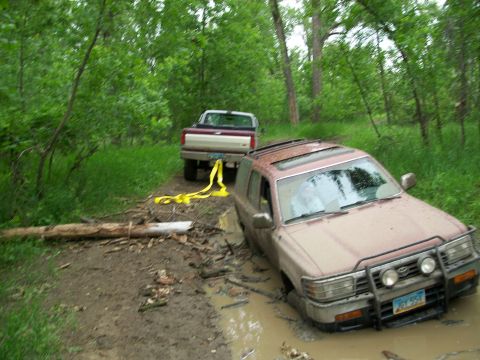 1988 Ford F-150 - Two trucks are on a muddy trail, one SUV is stuck and the other is pulling it out.