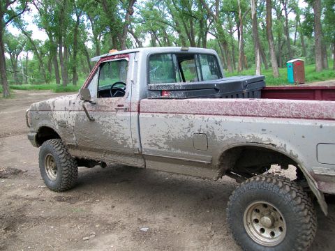 1988 Ford F-150 - This heavily muddied Ford pickup truck is viewed from the side, showing its worn condition and off-road tires.