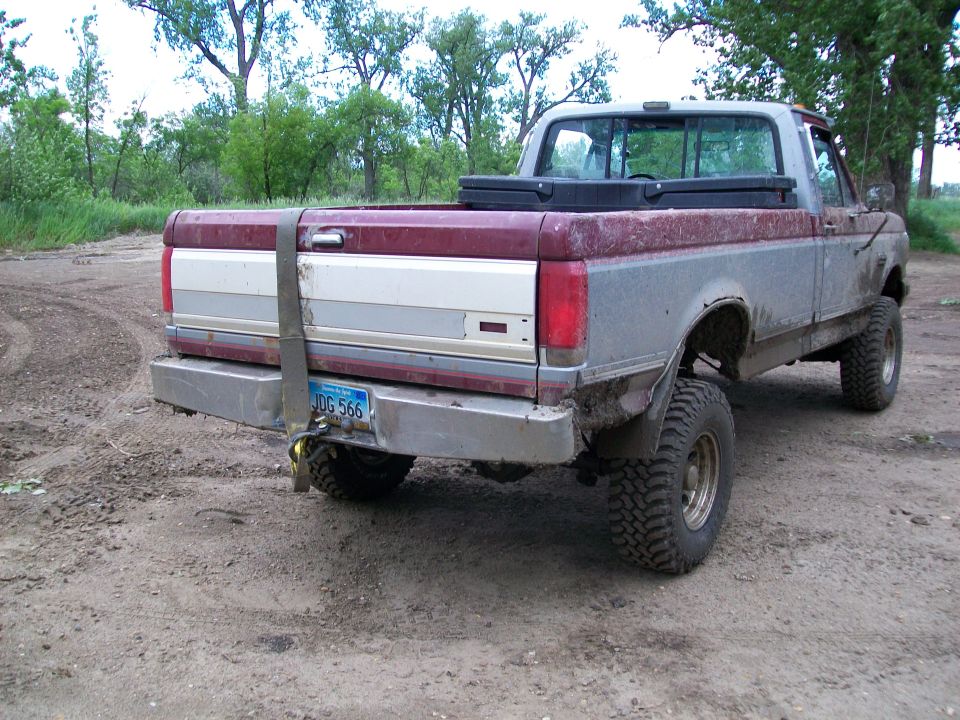 Rear view of a red and silver pickup truck with a strap on the tailgate and a license plate reading JDG 566