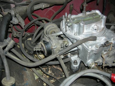 1979 Ford Bronco - Engine compartment detail showing a carburetor and various hoses, with a red painted background.