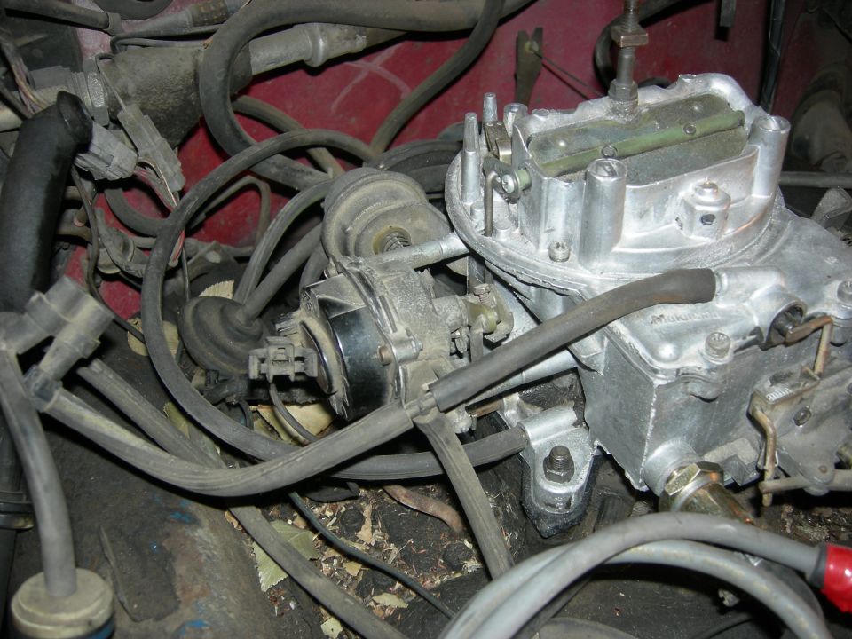 Close-up of a carburetor and engine hoses, red engine bay visible