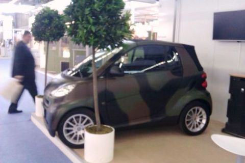 1991 Ford Crown Victoria - A Smart Fortwo with a camouflage wrap is displayed indoors.