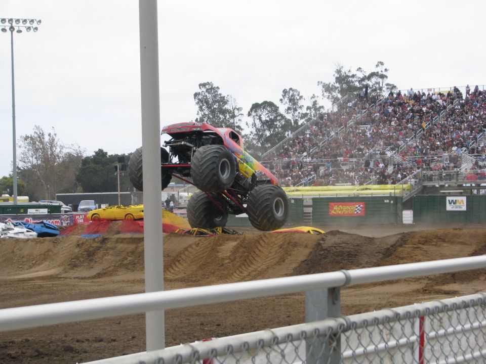 Monster truck mid-air over crushed cars, crowd in stadium seats
